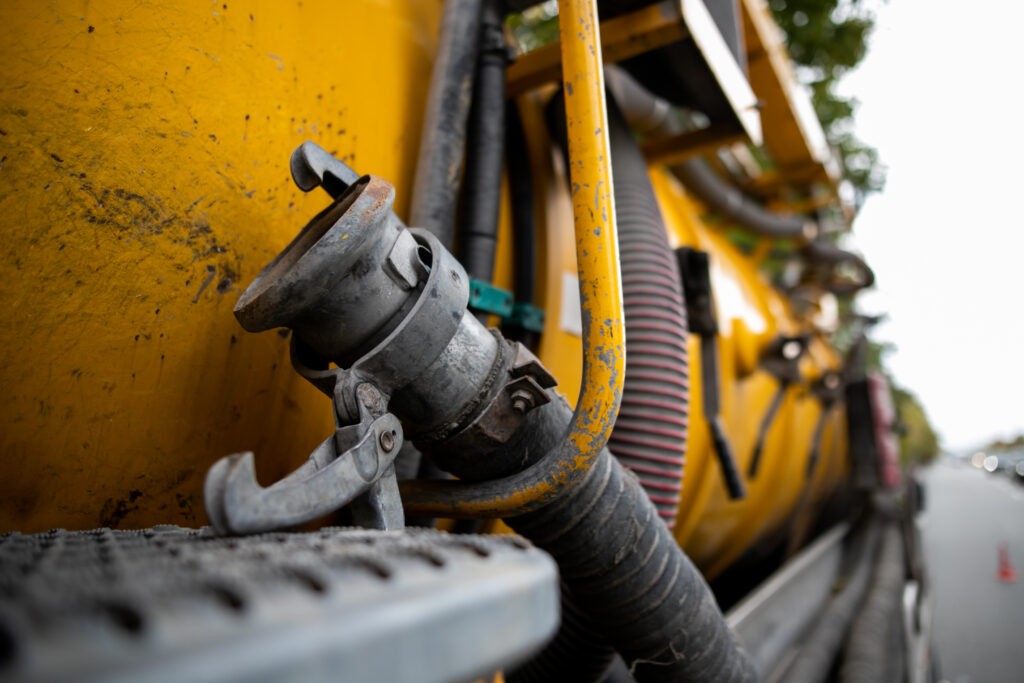 Side view of powerful professional modern yellow sewage sewerage truck working near a house pumping basement canalisation water.